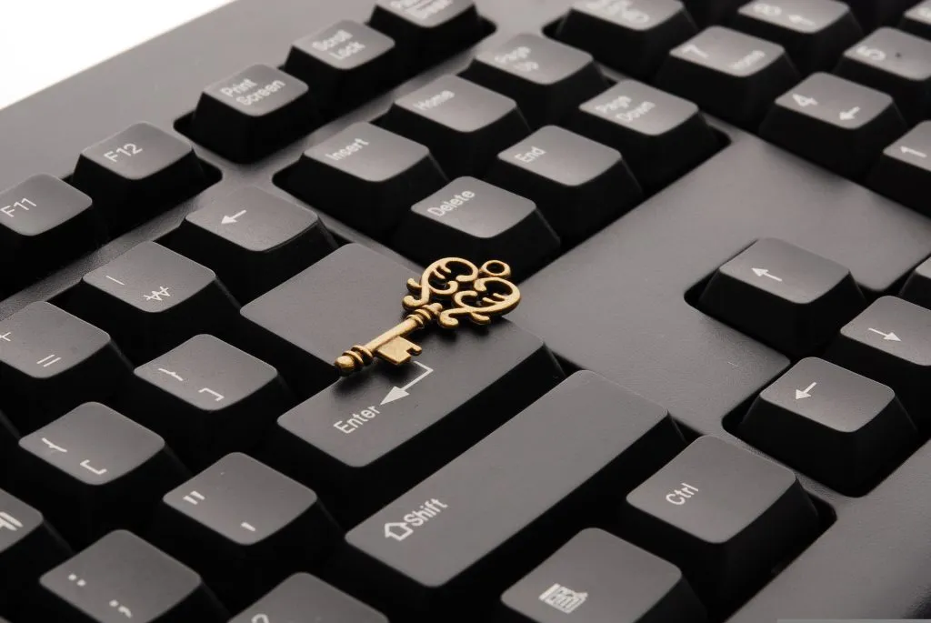 A high-angle, close-up photo shows a small, ornate, antique-style brass key resting horizontally across the Enter key of a modern, matte black computer keyboard.