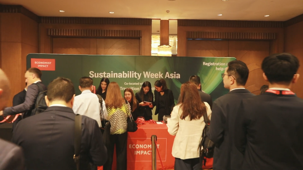 People line up to register in an event with 4 registrants standing in front of a 'Sustainable Week Asia' screen behind them.