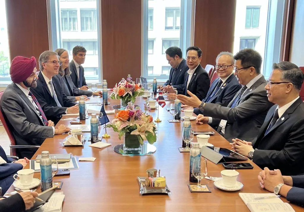 Two groups of men and women in formal suits sit facing each other at a long wooden table for a high-level diplomatic meeting.