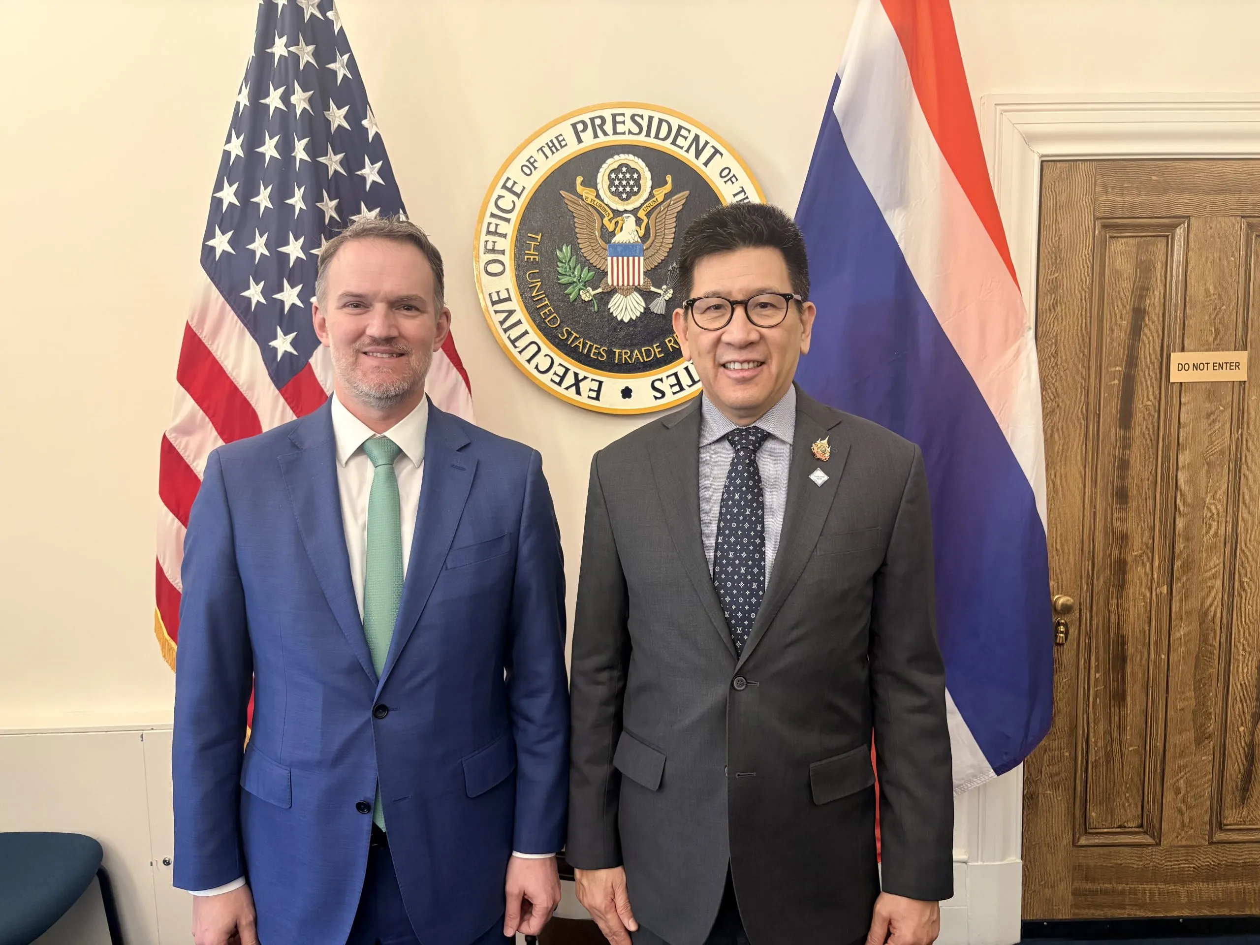 Two men stand side-by-side in a formal office between the US and Thai flags, beneath the seal of the Executive Office of the President.
