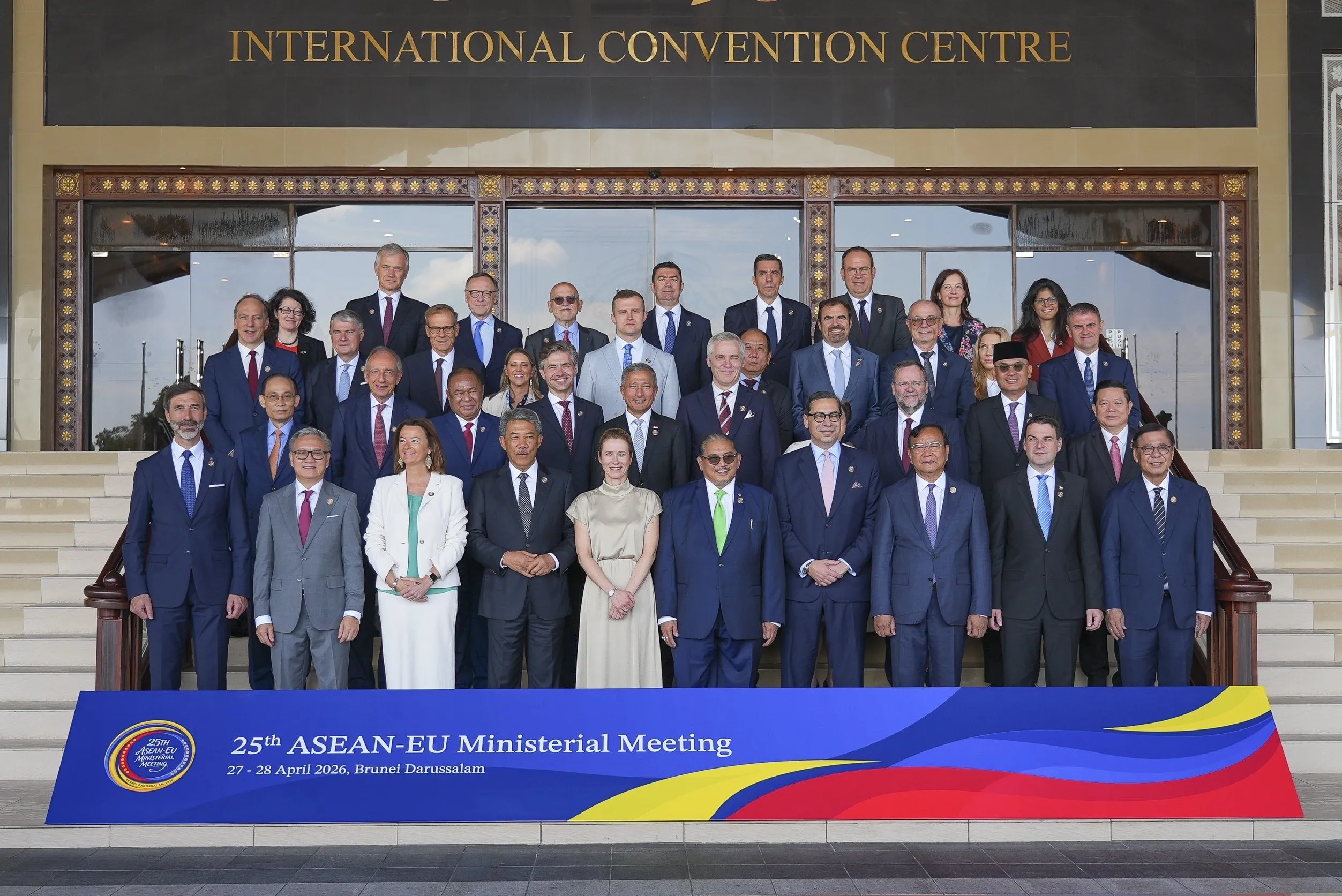 A large group of diverse diplomats in formal attire pose for a group photo in front of the International Convention Centre for a ministerial meeting.