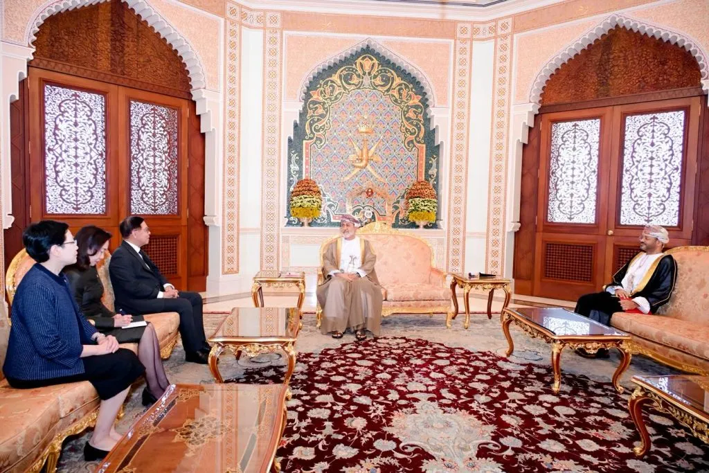 An Asian delegation in formal attire sits across from Omani officials in an ornate, arched room featuring intricate mosaics and golden furniture on a large rug.