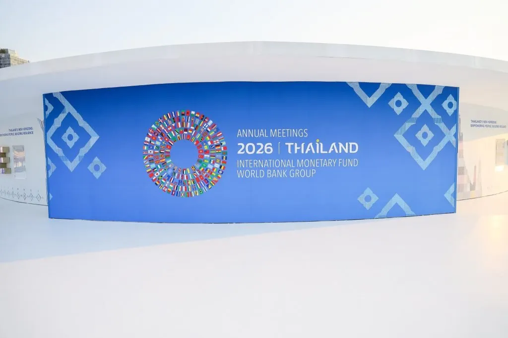 A curved blue wall features a colorful flag circle and text announcing the 2026 IMF World Bank Annual Meetings.