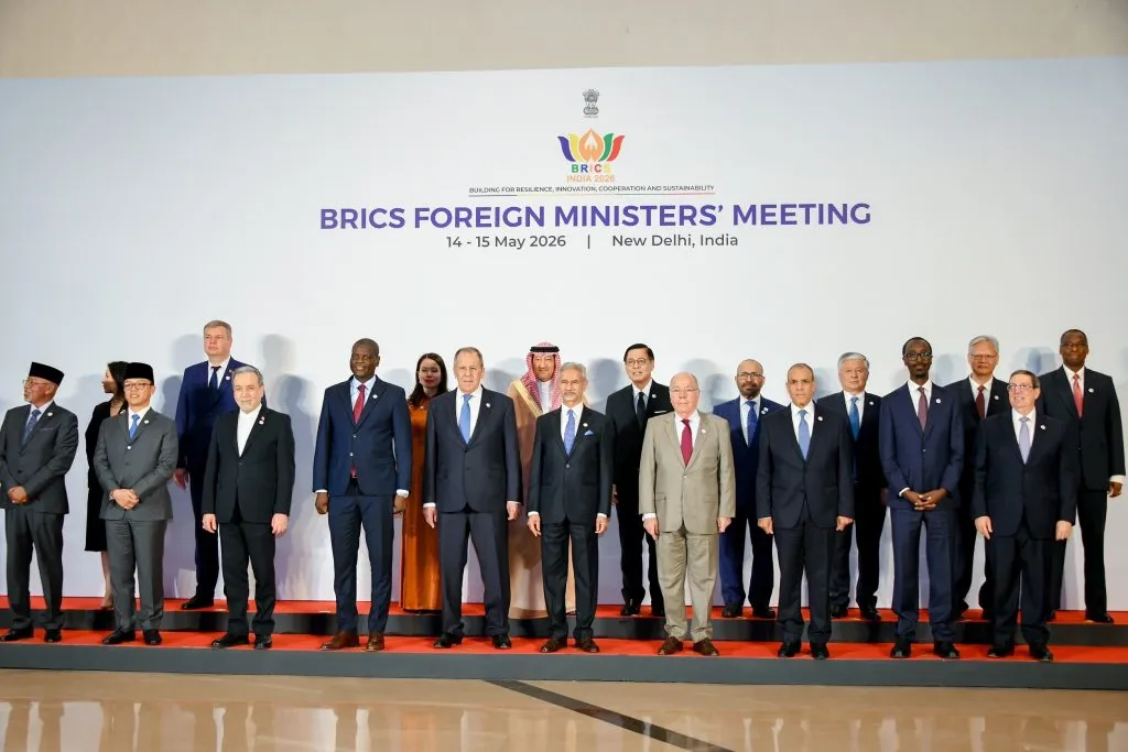A formal group photo shows over a dozen world leaders and ministers standing in a line against a white BRICKS summit backdrop.