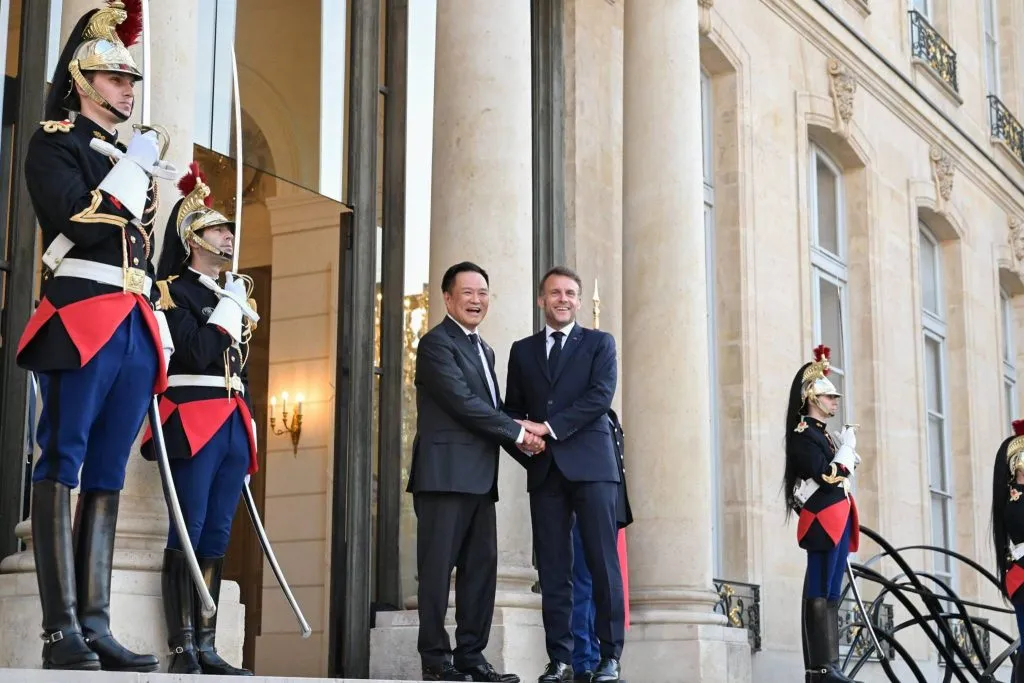 Officials shake hands on steps flanked by uniformed guards.