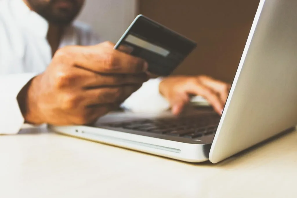 A man's hands use a laptop while holding a credit card for an online purchase.