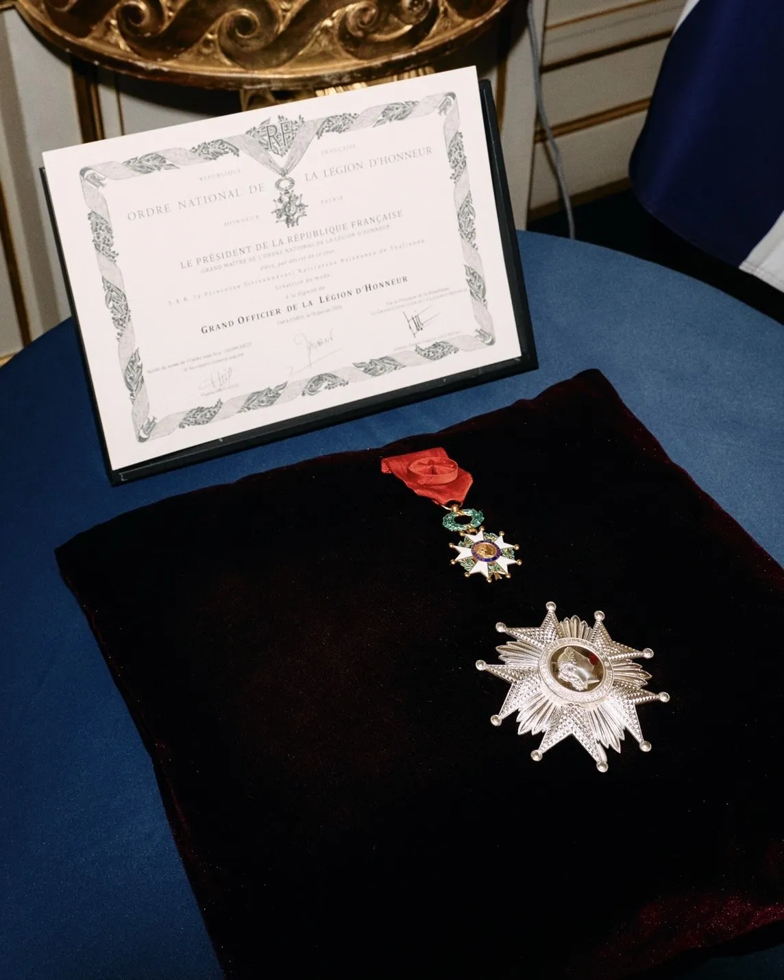 A close-up of a white certificate and a velvet cushion holding a silver star medal and a smaller medal attached to a red ribbon.