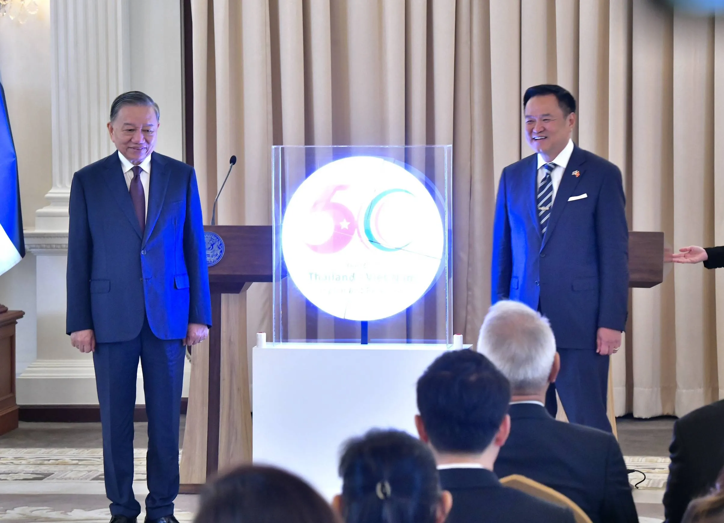 Two men in suits stand smiling beside a glowing circular display showing the number fifty.