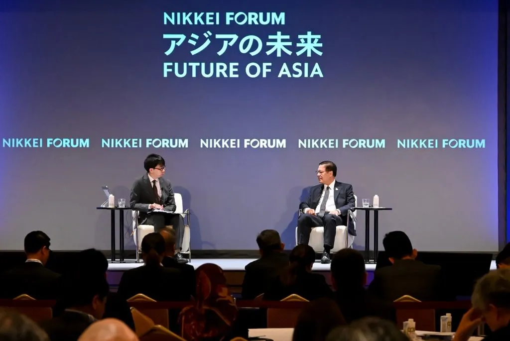 Two men in suits sit on a stage during an interview for a Nikkei Forum event.