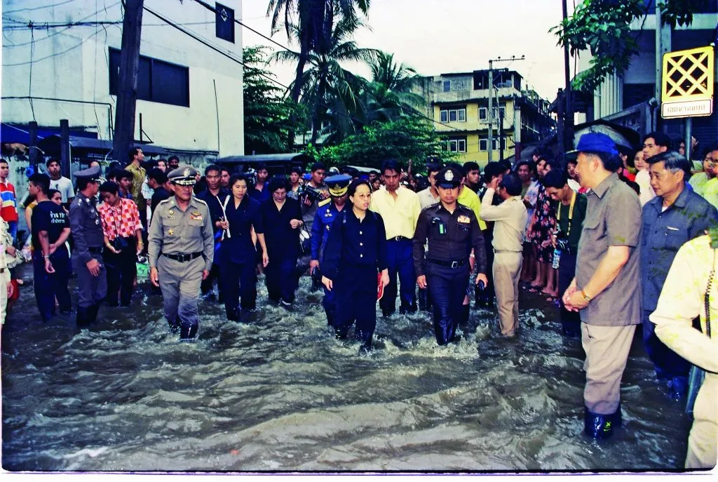 Officials and a crowd wade through a flooded city street.