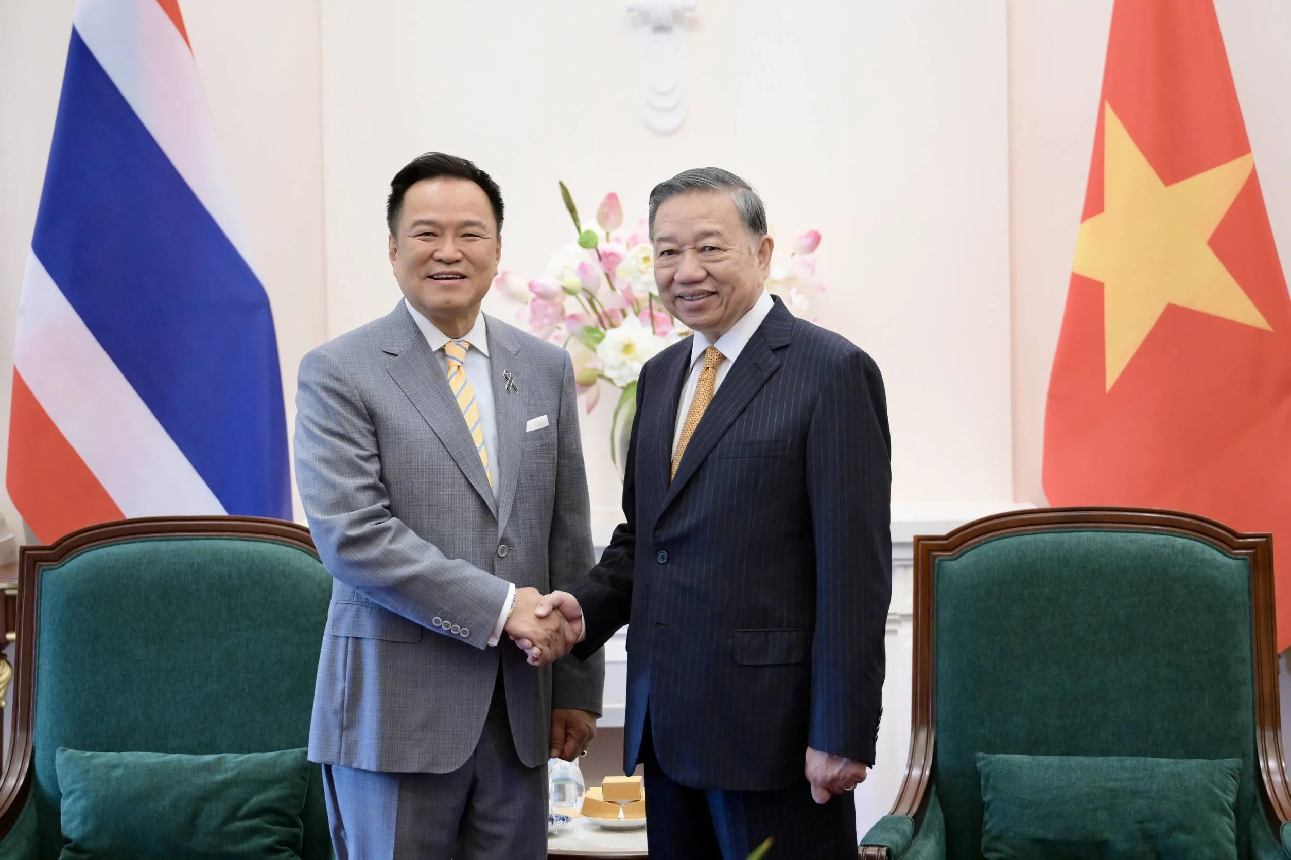 Two men in suit shaking hands in front of Thai and Vietnamese flags.