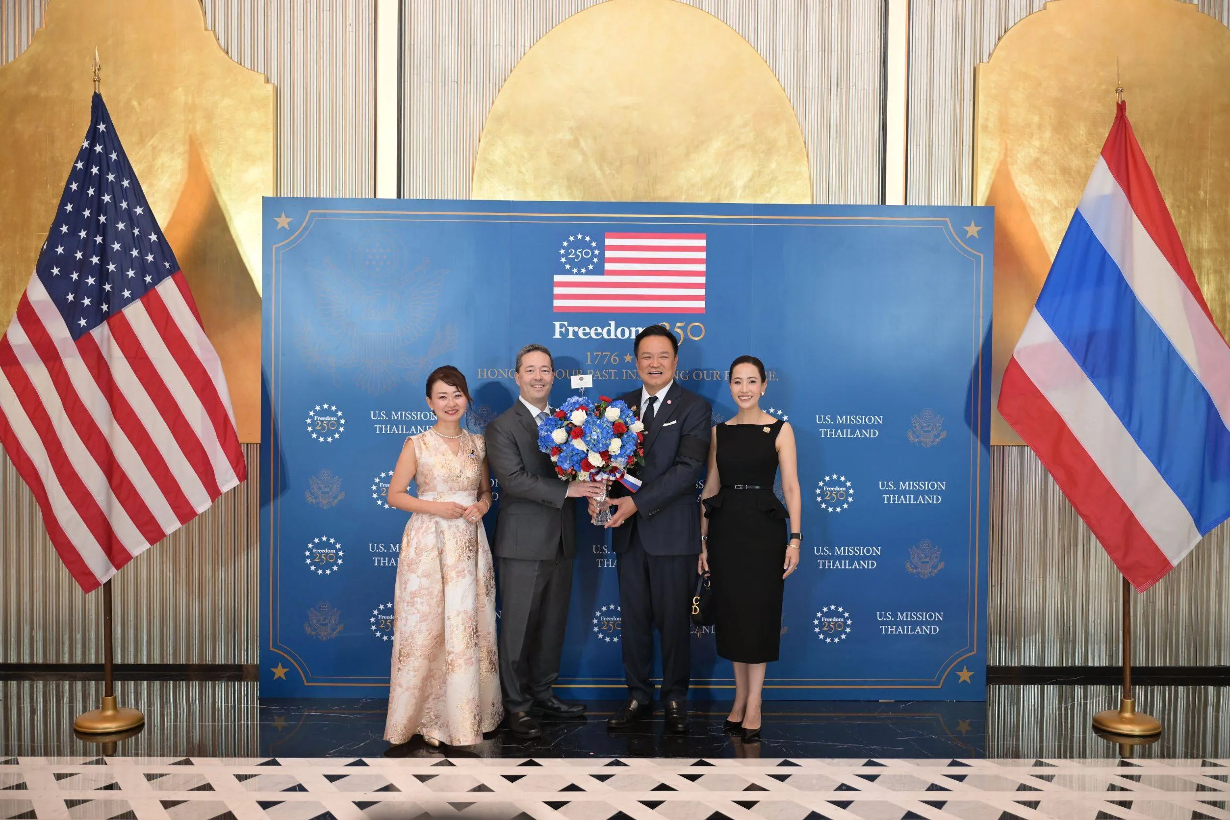 Ambassador Sean O'Neill and Prime Minister Anutin Charnvirakul hold a large floral bouquet with two women.