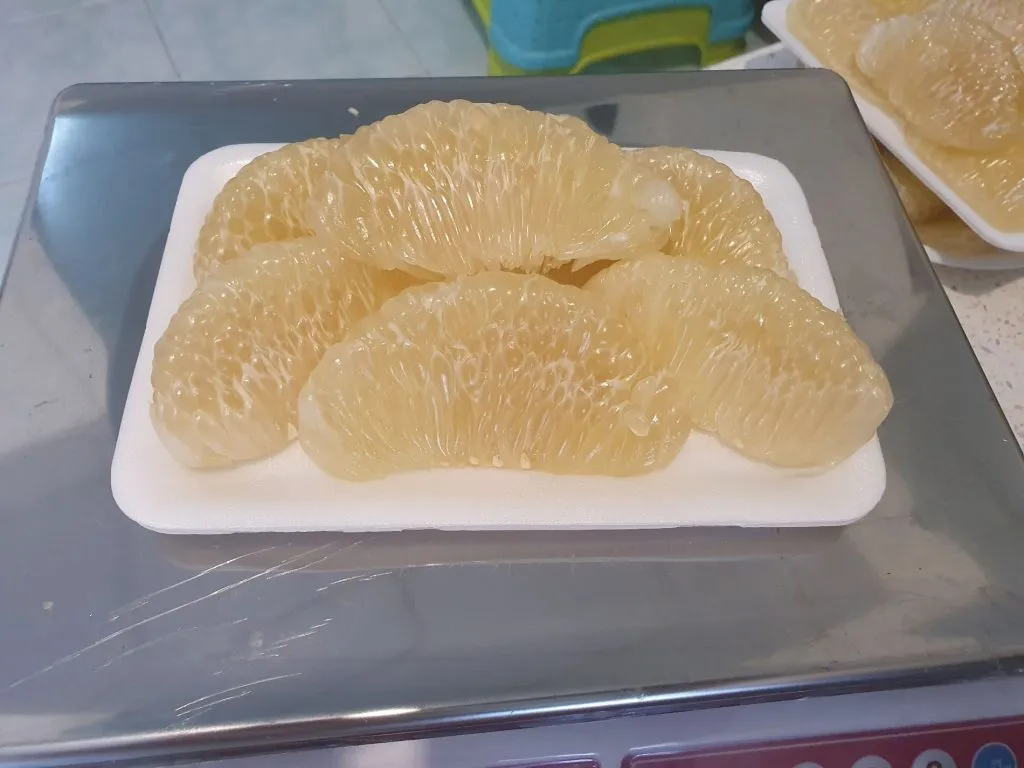 Several peeled, light-yellow citrus segments arranged neatly on a white rectangular tray.