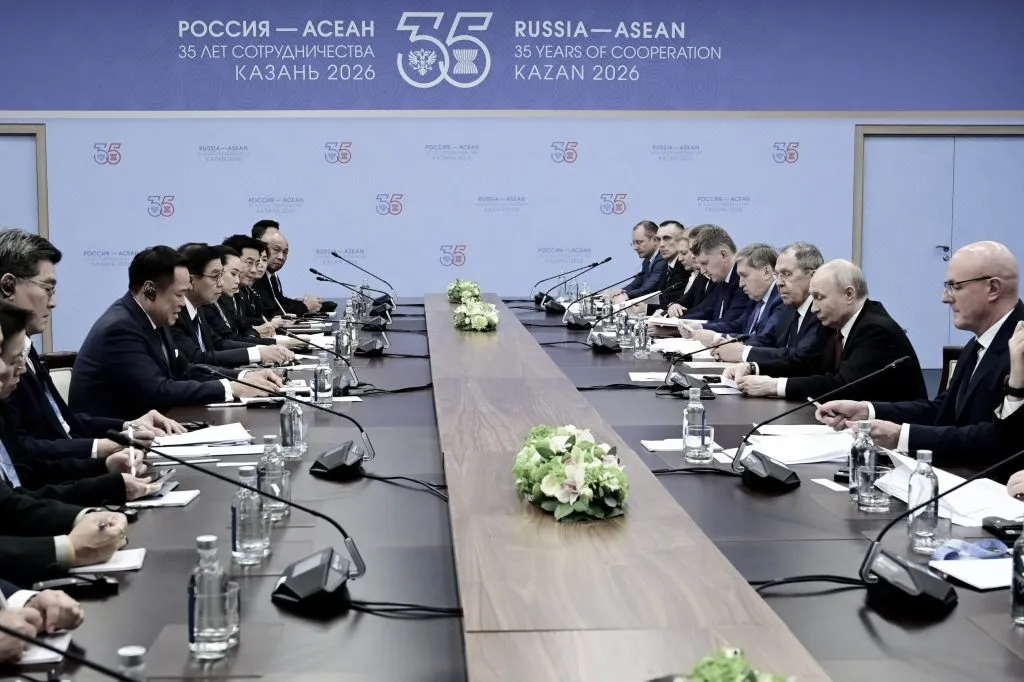 Two groups of people sitting on the opposite side of a long conference table, having a discussion.