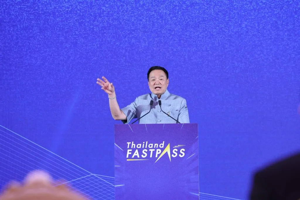 Prime Minister Anutin Charnvirakul stands at a purple "Thailand FASTPASS" podium, gesturing while speaking against a blue backdrop.