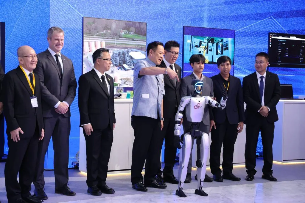 Prime Minister Anutin Charnvirakul points at a white humanoid robot standing among a group of men in suits.