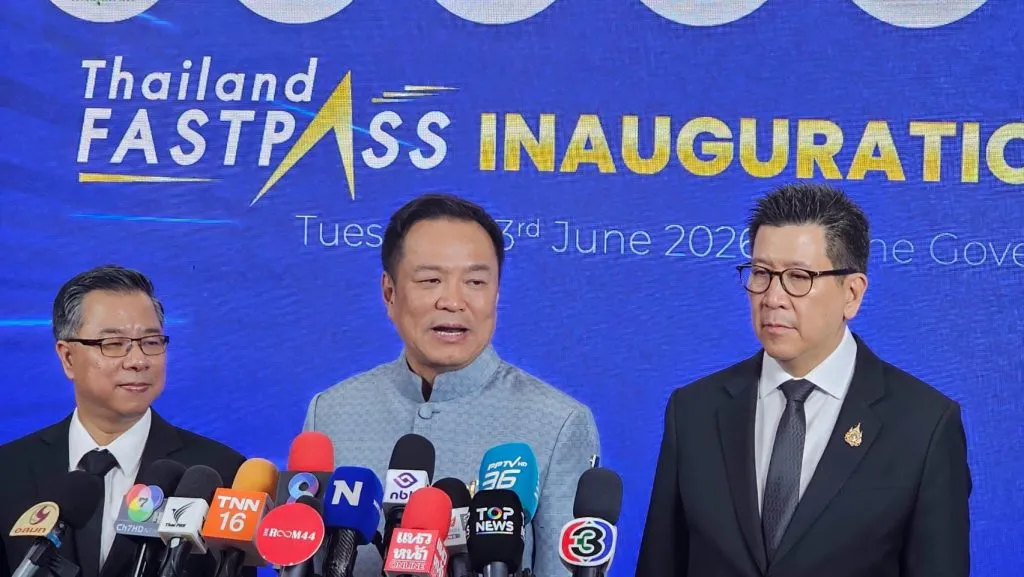 Prime Minister Anutin Charnvirakul speaks to a cluster of news microphones, flanked by two men in dark suits.