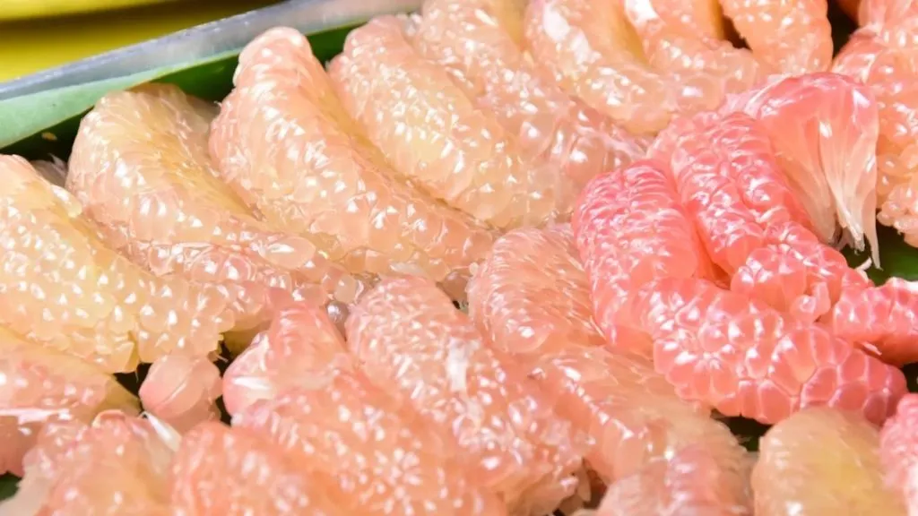 A close-up view of numerous juicy pink and yellow citrus segments packed tightly together.