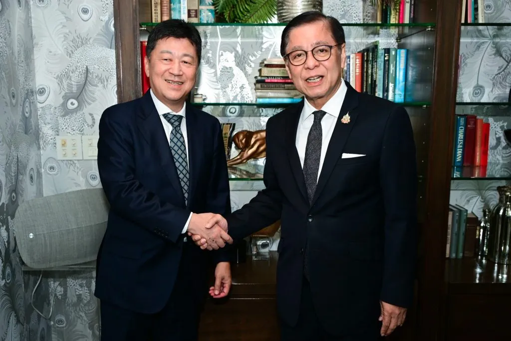 H.E. Mr. Sihasak Phuangketkeow smiles warmly while shaking hands with a delegate in a room.