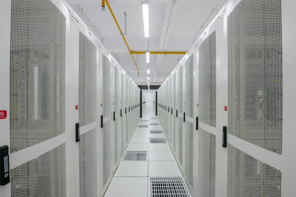 A long hallway lined with tall white server cabinets featuring perforated mesh doors on both sides.