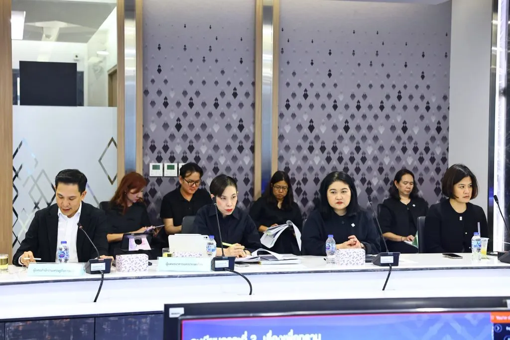 Several professional attendees sit in a row at a meeting table with microphones in front.