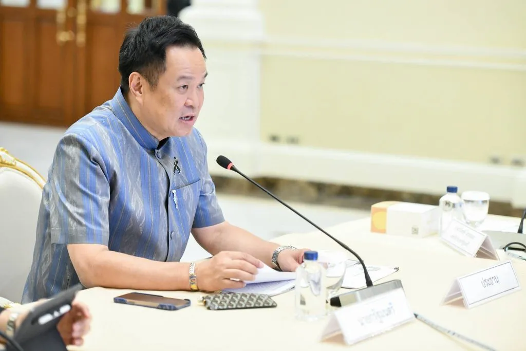 Thai Prime Minister Anutin Charnvirakul speaks into a microphone while referring to document papers during a formal meeting.