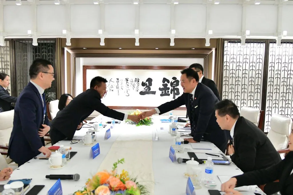 Prime Minister Anutin Charnvirakul shakes hands across a conference table during a meeting in Beijing.