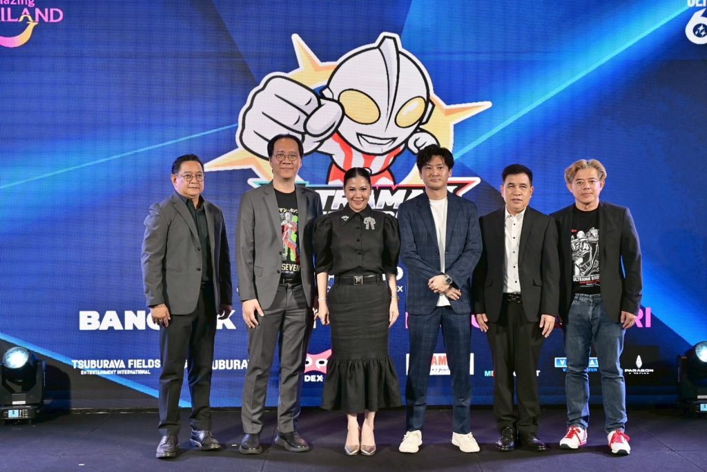 Six people stand in a row on a stage in front of a large Ultraman banner.