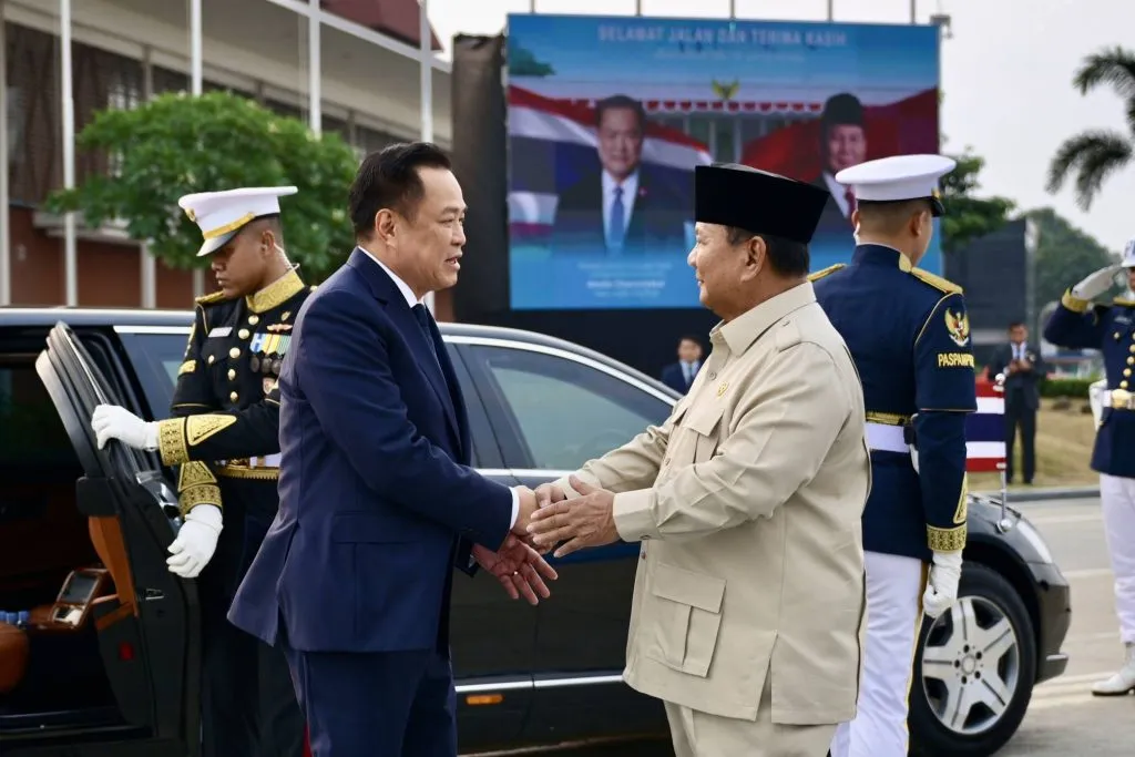 Thai Prime Minister Anutin Charnvirakul handshakes Indonesian President Prabowo Subianto upon arrival beside a luxury vehicle outdoors.