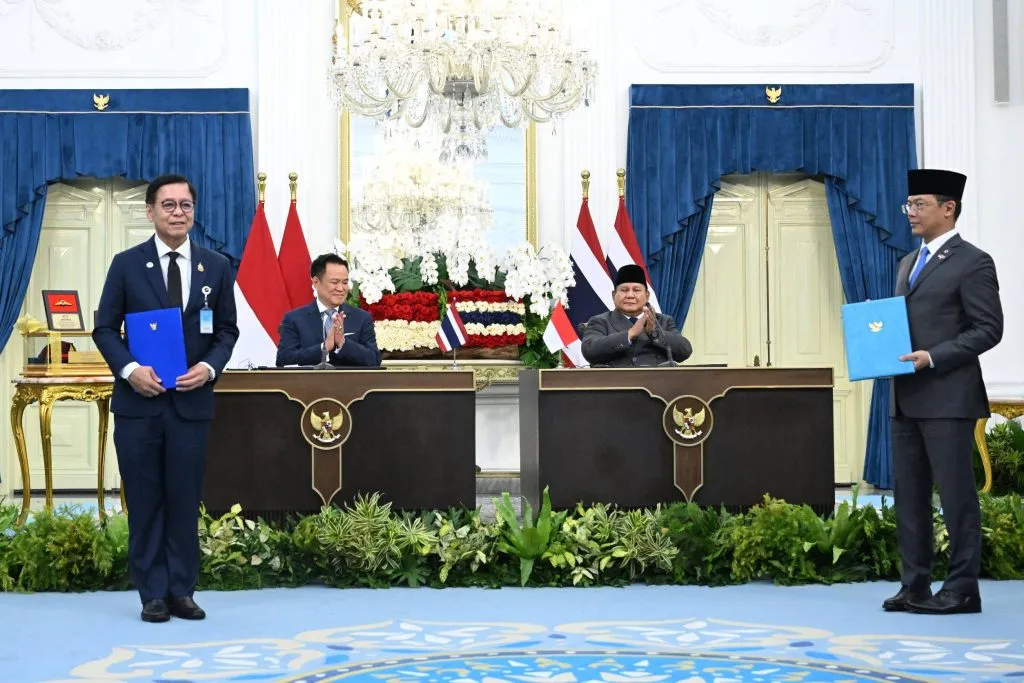 Anutin Charnvirakul and Prabowo Subianto applaud seated at desks during an official bilateral signing ceremony event.