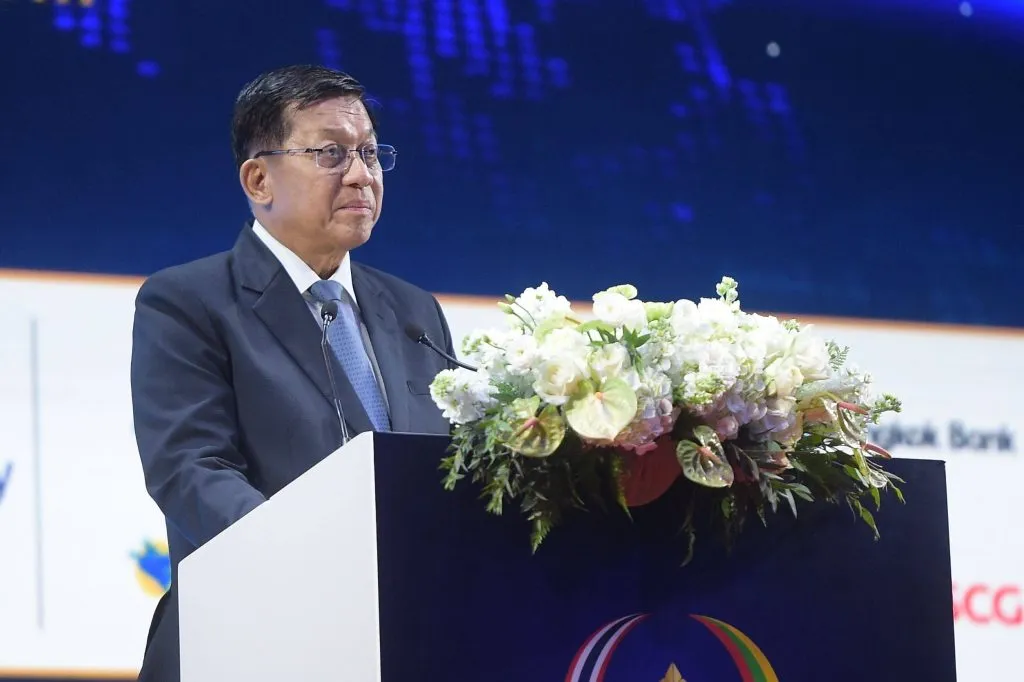 Min Aung Hlaing delivers a speech from a podium decorated with white flowers at a formal event.