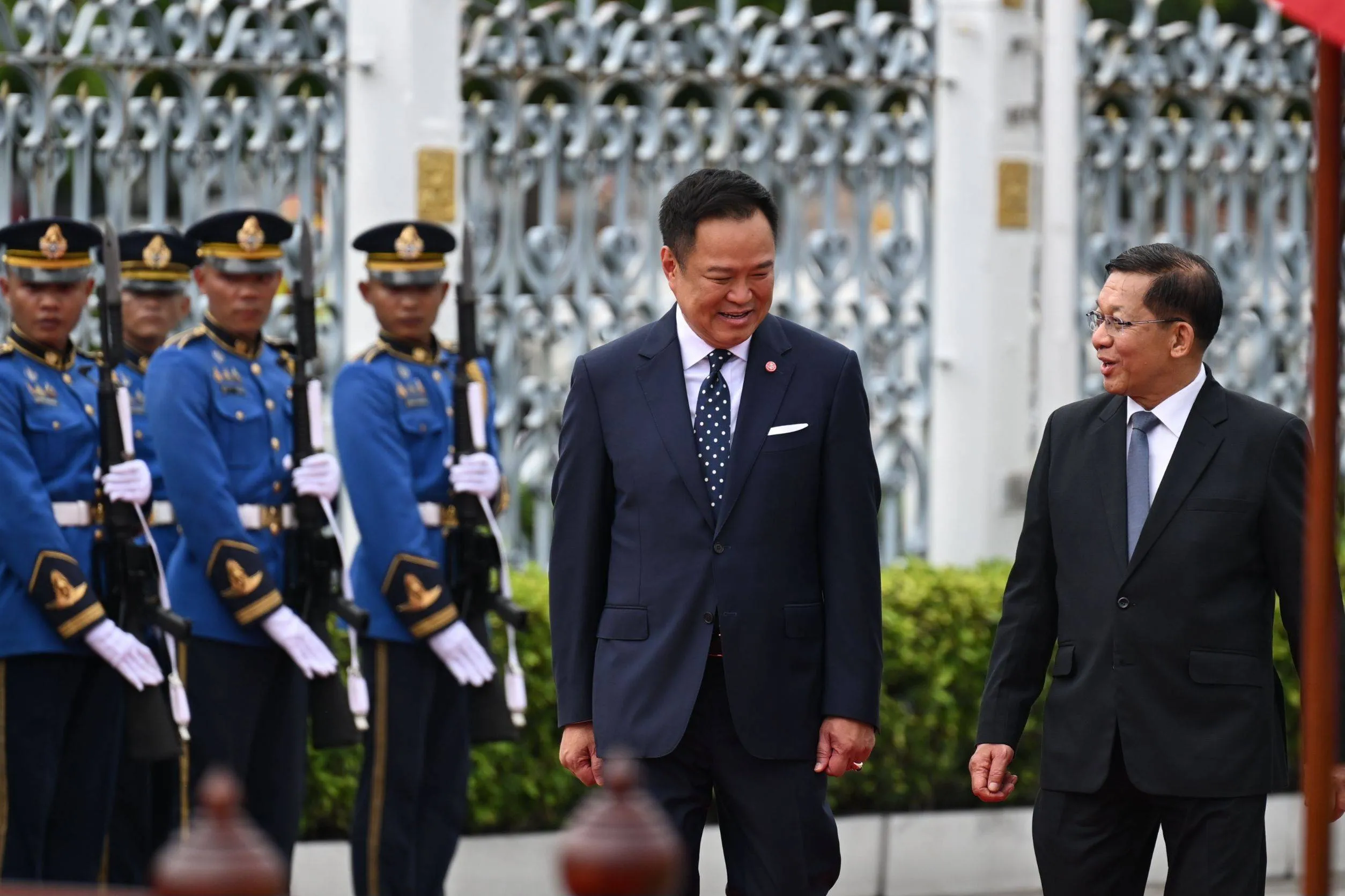 Anutin Charnvirakul and Min Aung Hlaing smile as they walk past soldiers standing in formation outdoors.