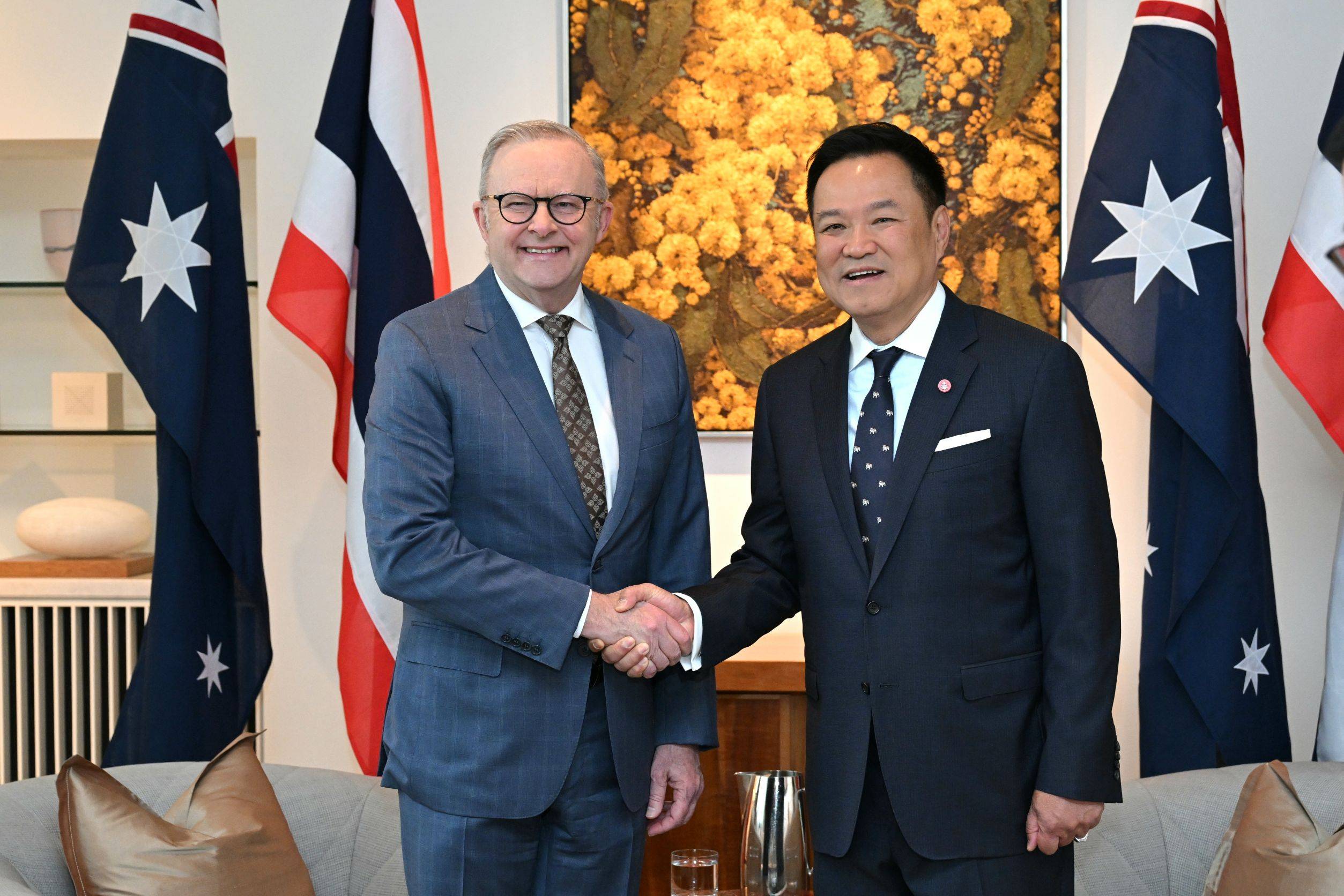 Thai and Australian prime ministers shake hands between national flags during an official bilateral meeting.