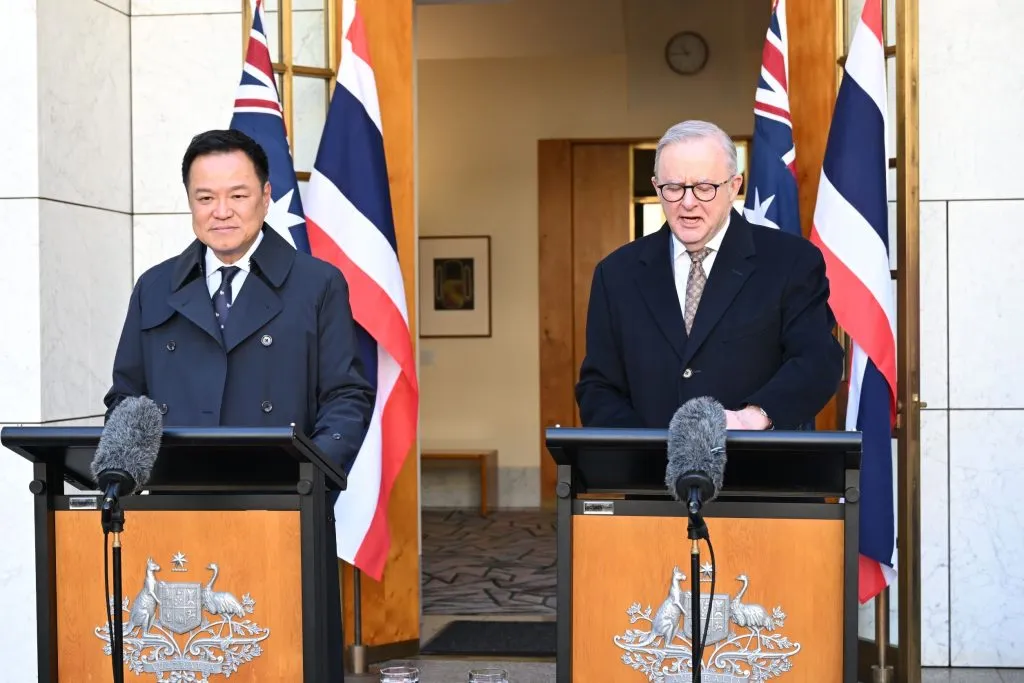 Thai and Australian prime ministers address reporters from separate lecterns framed by both countries' flags.