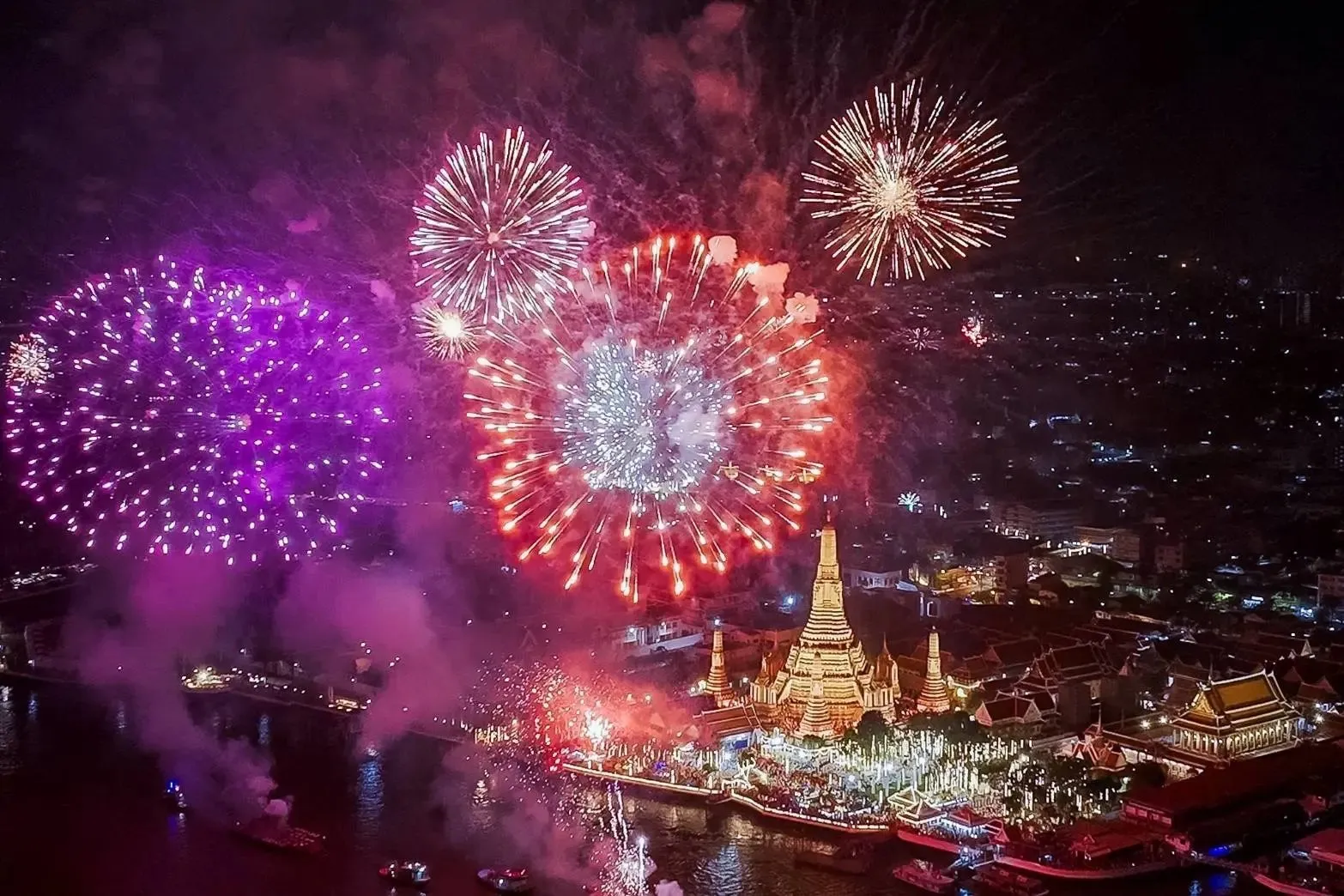 bird eye view of bangkok with temple and city landscape filling the horizon. the evening scene is lit up in multi-color fireworks