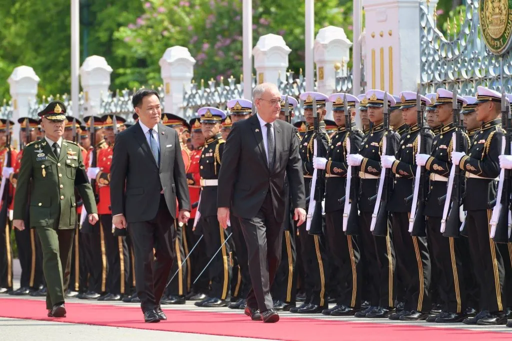 Thai Prime Minister Anutin Charnvirakul and Swiss President Guy Parmelin walk along a red carpet past a row of guards of honor.