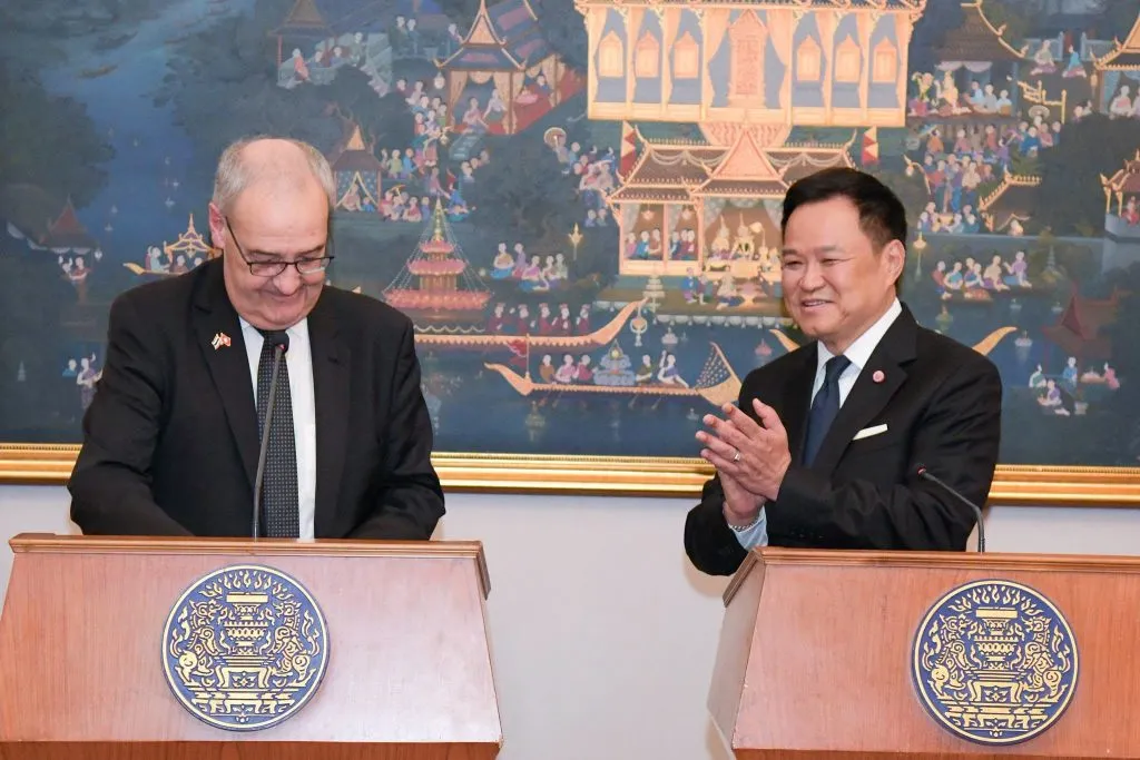 Thai Prime Minister Anutin Charnvirakul and Swiss President Guy Parmelin stand behind official wooden lecterns while one is clapping his hands.