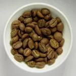 Roasted coffee beans fill a white bowl in a close-up view.
