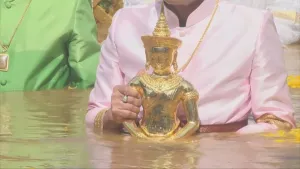 A participant holds a small golden Buddha image in the river during a submersion ceremony.